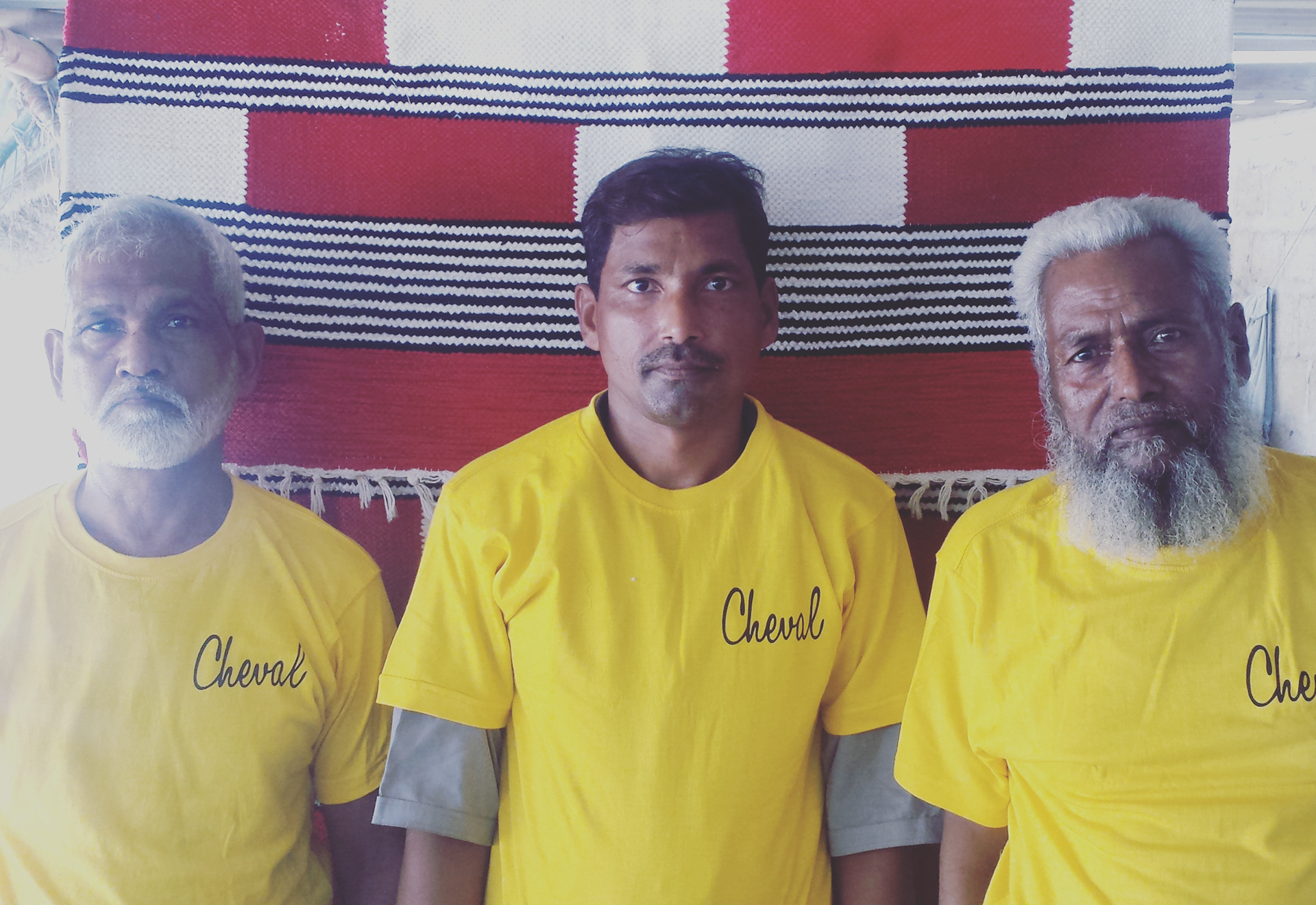 Three Cheval Rugs craftspeople wearing branded yellow shirts in front of a woven rug