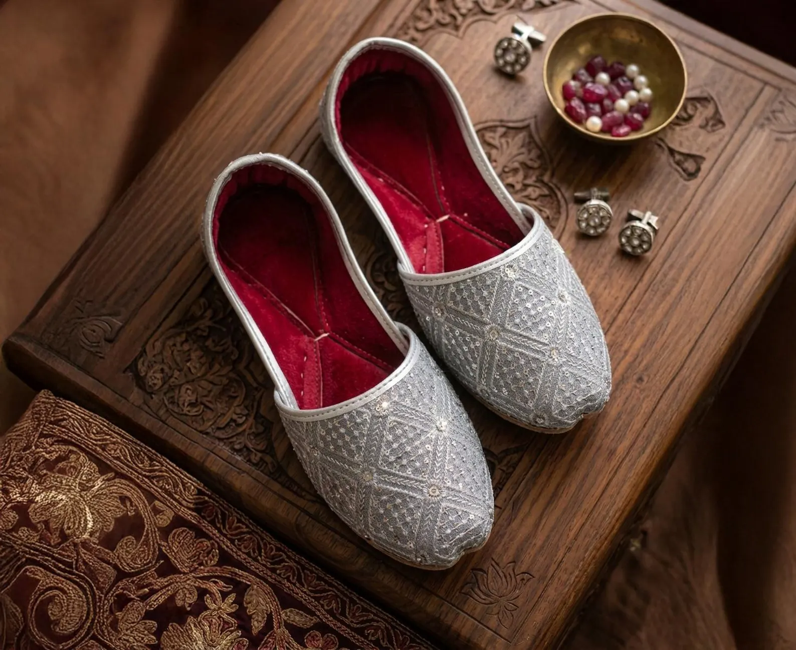 Silver embroidered juttis with red interiors on a carved wooden table
